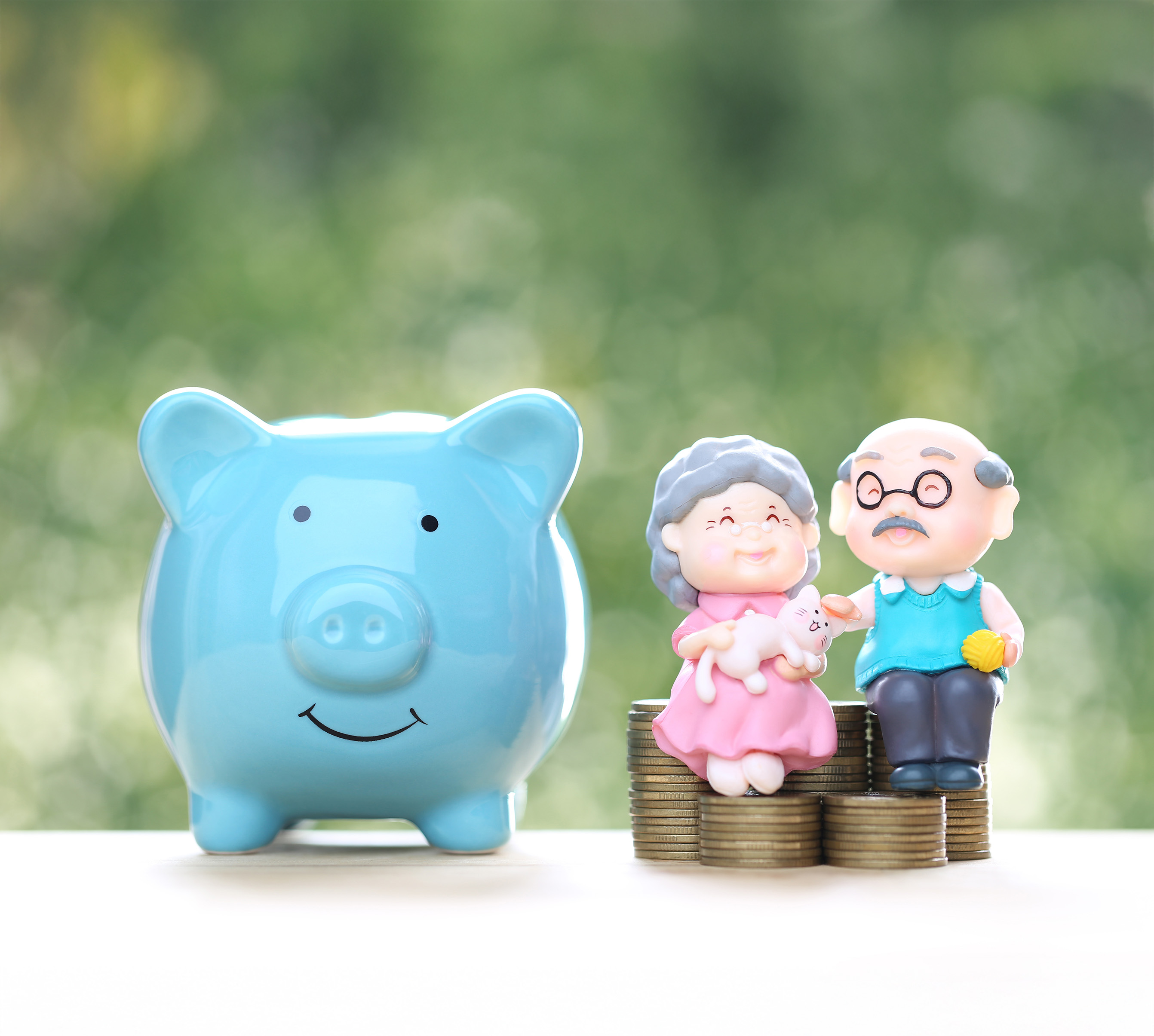 Glückliches Rentnerpaar sitzt auf Münzstapeln neben einem blauen Sparschwein – Symbol für Altersvorsorge und finanzielle Sicherheit im Alter.