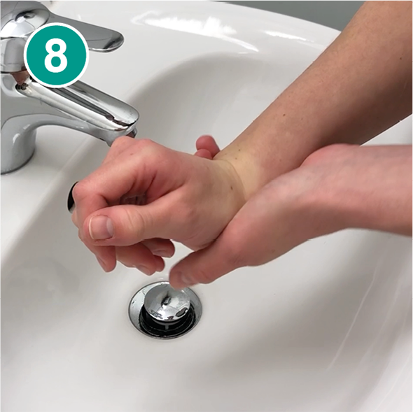Nahaufnahme von zwei Händen über einem weißen Waschbecken im achten Schritt des Händewaschens. Die rechte Hand umfasst das Handgelenk der linken Hand, um es gründlich zu reinigen. Im Hintergrund ist ein silberner Wasserhahn zu sehen. Oben links im Bild befindet sich ein grüner Kreis mit der weißen Zahl „8“, der den achten Schritt einer Händehygiene-Anleitung kennzeichnet.